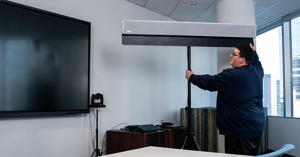 An IT specialist positions an HDL310 audio conferencing system on a stand in a meeting room.